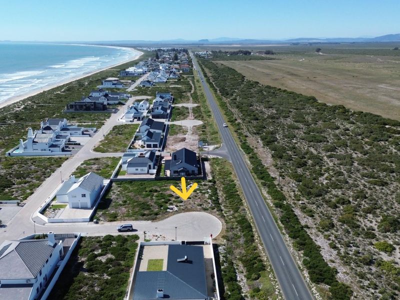 Aerial view of a vacant residential plot situated in a coastal development, offering proximity to the beach and main road access.
