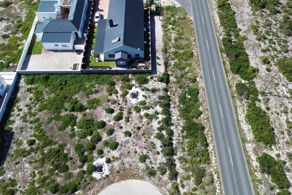 Aerial view of a vacant residential plot situated adjacent to a paved road and established residential properties.