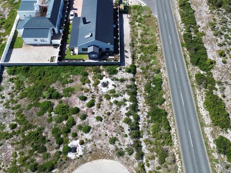 Aerial view of a vacant residential plot situated adjacent to a paved road and established residential properties.