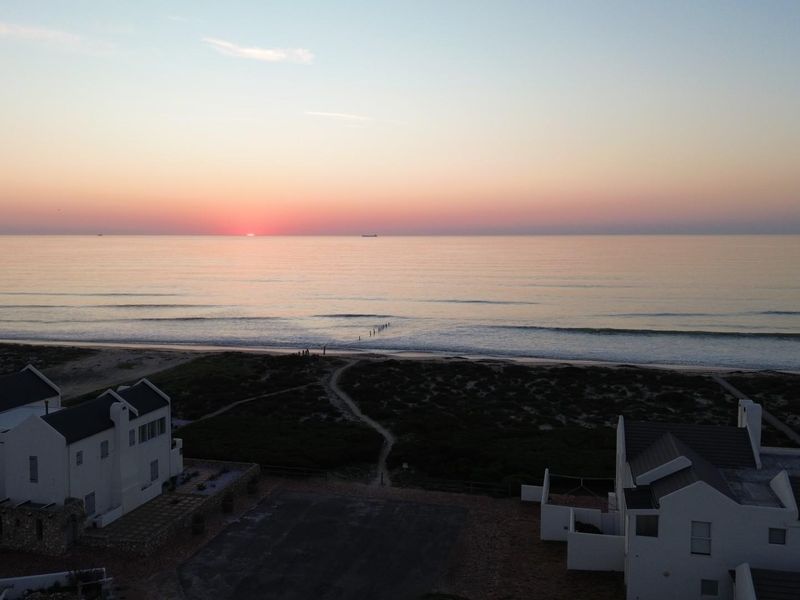 Aerial view of a coastal residential property featuring direct beach access and scenic ocean views at sunset.