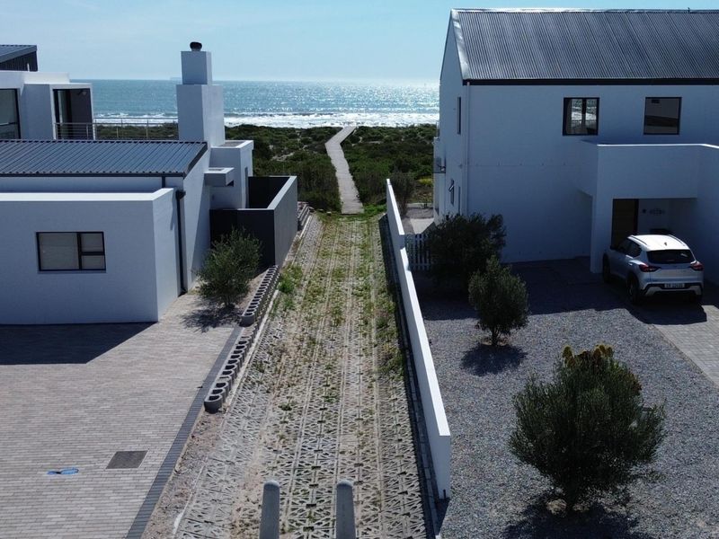 Aerial view of a residential property featuring a paved driveway, gravel landscaping, and a direct boardwalk path leading toward the ocean.