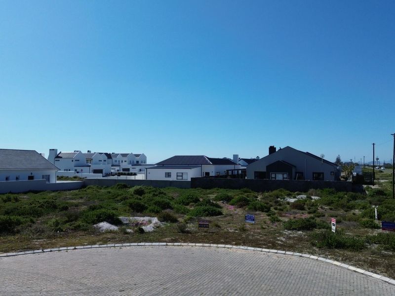 An aerial view of a vacant residential plot situated in a developed estate, featuring a paved cul-de-sac and surrounding established homes.