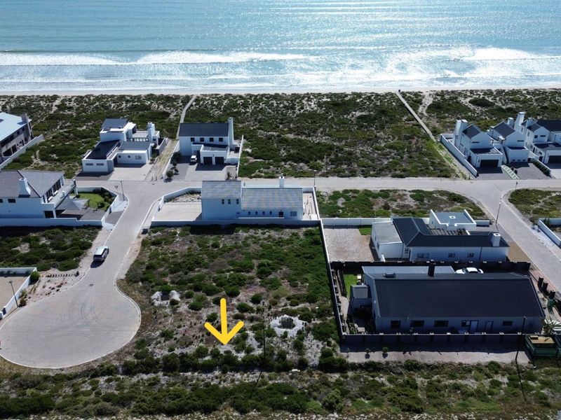 Aerial view of a vacant residential plot situated in a coastal estate, featuring direct access to paved roads and proximity to the beach.
