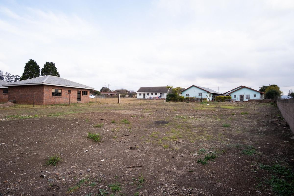 A view of a large, undeveloped residential plot with surrounding neighboring properties and perimeter boundary walls.