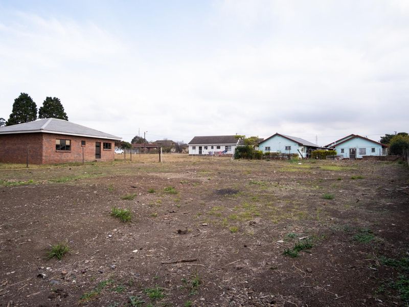 A view of a large, undeveloped residential plot with surrounding neighboring properties and perimeter boundary walls.