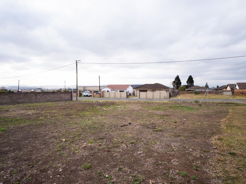 A vacant residential plot of land featuring a boundary wall, utility pole, and overhead power lines in a suburban neighborhood setting.
