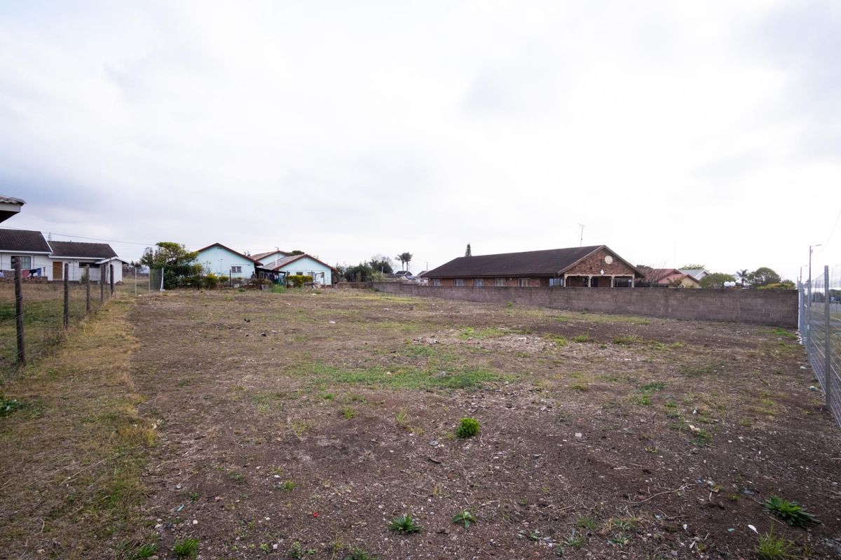 A vacant residential plot featuring perimeter fencing and a boundary wall, situated in an established neighborhood setting.