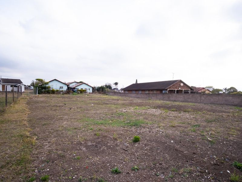 A vacant residential plot featuring perimeter fencing and a boundary wall, situated in an established neighborhood setting.