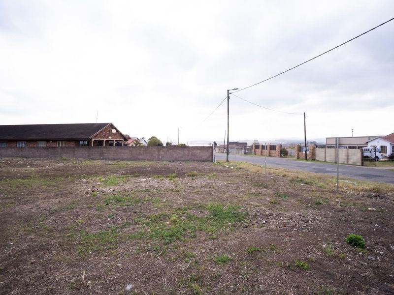 A vacant residential plot of land featuring a boundary wall, adjacent to a paved street with utility infrastructure.
