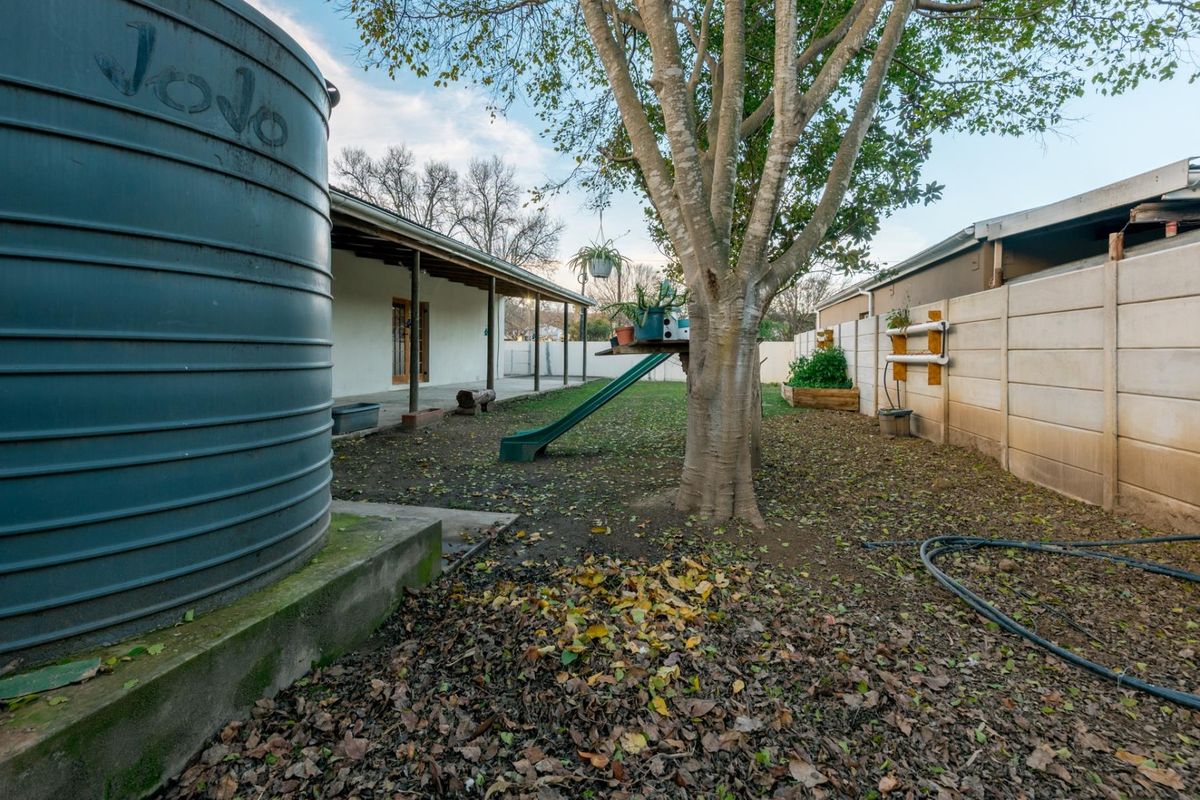 Rear garden area featuring a large water tank, a covered patio, and a concrete boundary wall, offering potential for landscaping and outdoor improvement.