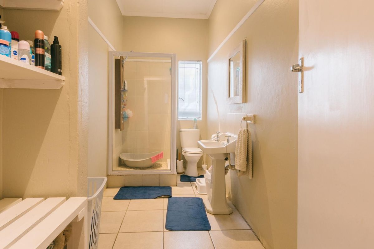A functional bathroom featuring a pedestal sink, a shower enclosure, and a toilet, finished with neutral wall tones and tiled flooring.