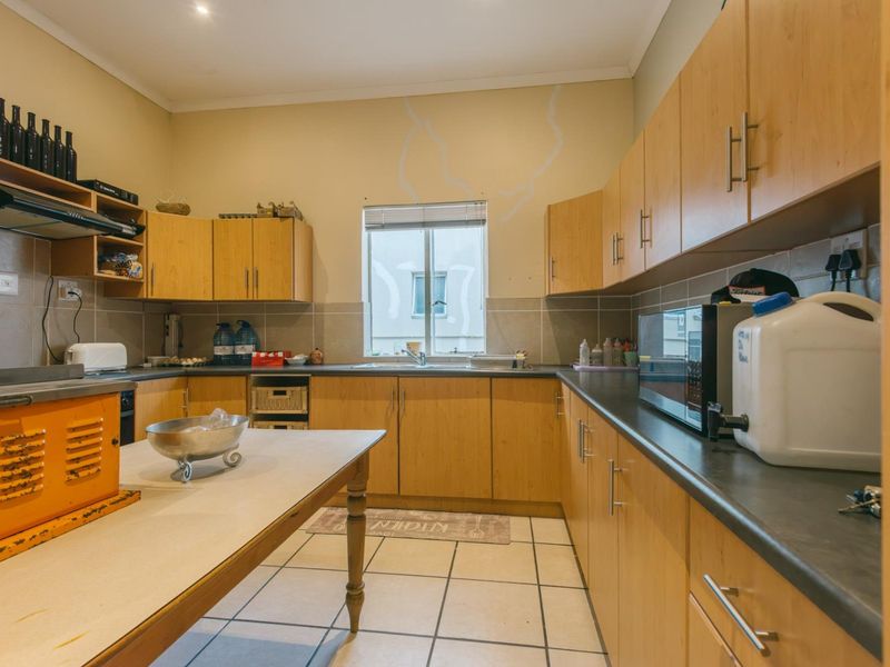 A functional kitchen featuring light wood-finish cabinetry, dark countertops, tiled flooring, and a central prep area with integrated appliances.