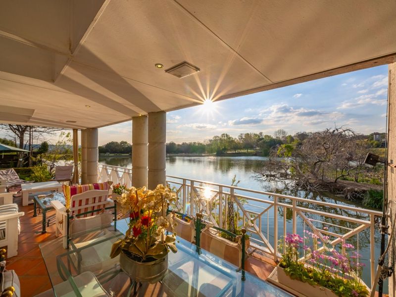 A spacious covered patio featuring terracotta tiling and metal balustrades, offering expansive views over the adjacent lake.