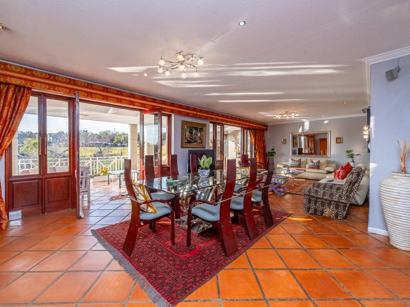 Spacious open-plan living and dining area featuring terracotta flooring, recessed lighting, and large glass doors opening onto a covered patio.