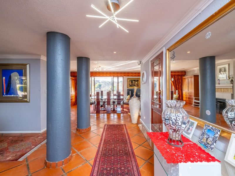 Spacious open-plan living area featuring terracotta floor tiles, structural columns, and a large wall mirror, creating a bright and connected interior space.