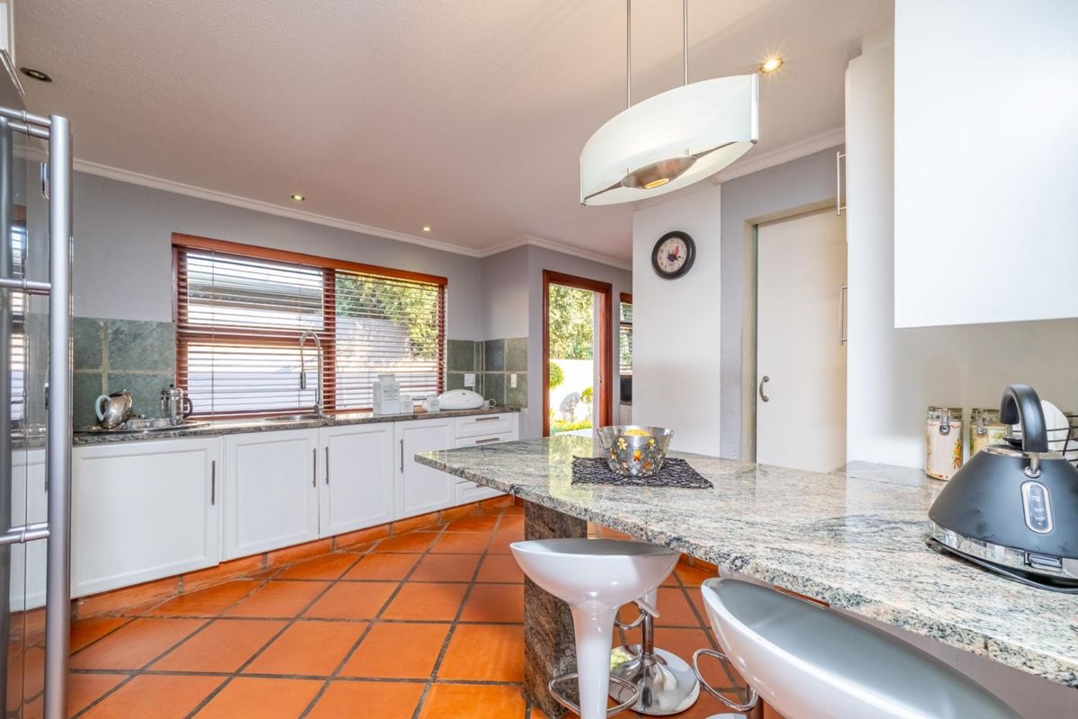 A well-lit kitchen featuring granite countertops, white cabinetry, terracotta flooring, and a breakfast bar, offering a functional and inviting culinary space.