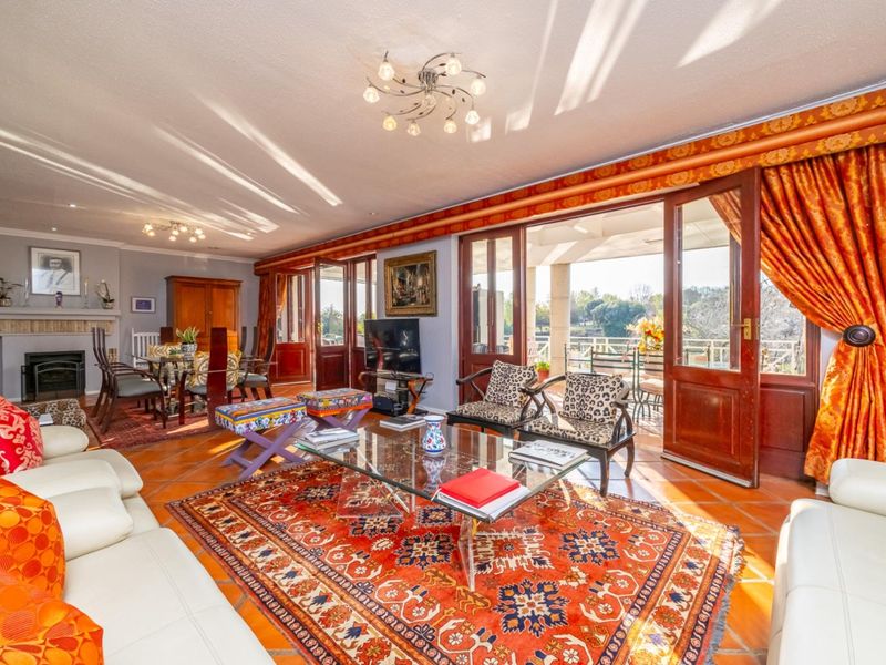 Spacious open-plan living and dining area featuring terracotta flooring, a fireplace, and large wooden doors opening onto an outdoor patio.