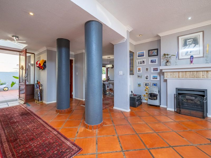 Spacious living area featuring terracotta floor tiles, a built-in fireplace, and structural columns, with natural light flowing from an adjacent entrance and skylight.