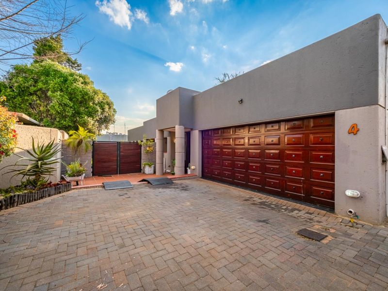 Front elevation of the property featuring a paved driveway, a large wooden double garage door, and a secure pedestrian gate entrance.