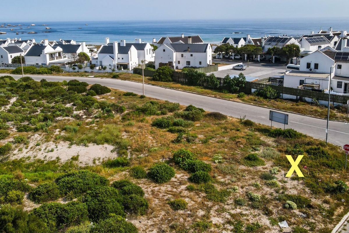 Aerial view of a vacant residential plot situated in a coastal neighborhood, featuring natural vegetation and direct access to a paved street.