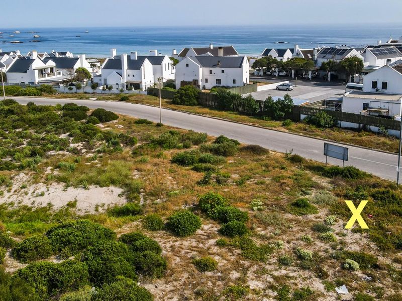 Aerial view of a vacant residential plot situated in a coastal neighborhood, featuring natural vegetation and direct access to a paved street.