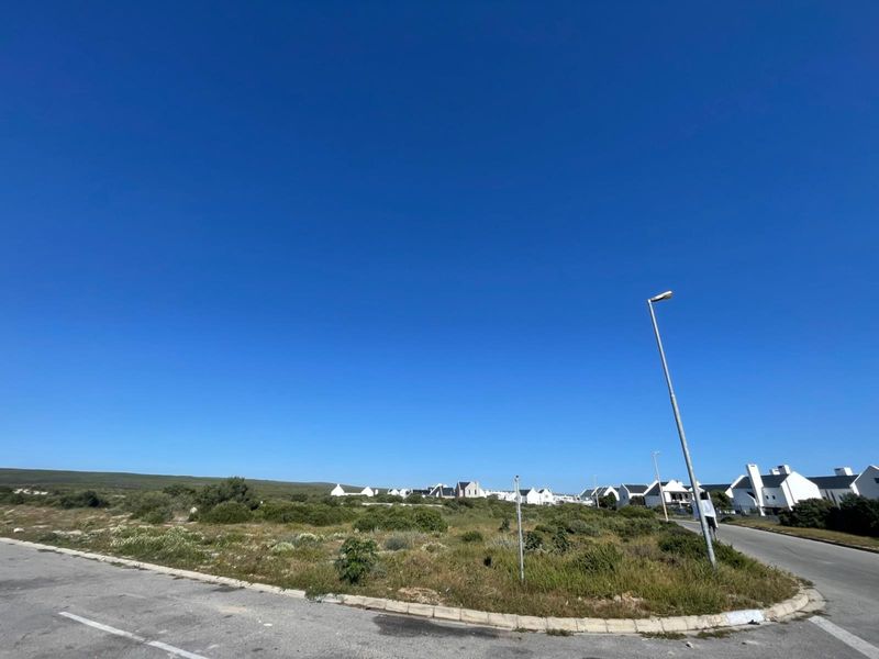 A view of a vacant residential plot situated on a corner lot with established street infrastructure and surrounding residential development.