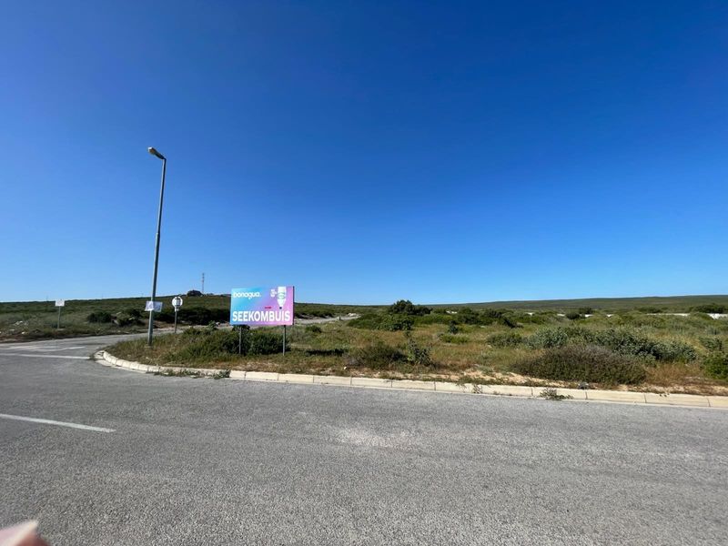 A view of the street frontage and surrounding vacant land area with a prominent signage board.