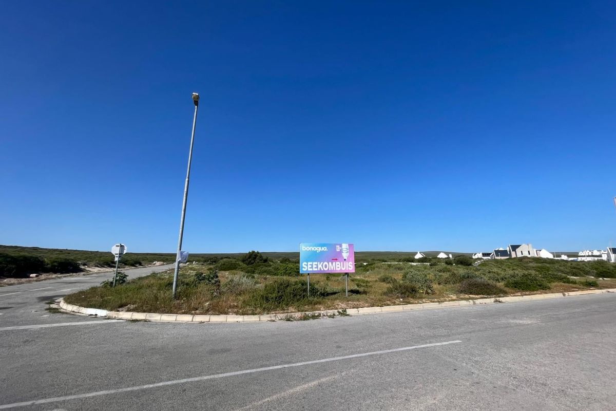 A view of a vacant residential plot situated on a corner lot, featuring paved road access and existing street lighting infrastructure.