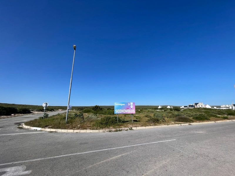 A view of a vacant residential plot situated on a corner lot, featuring paved road access and existing street lighting infrastructure.