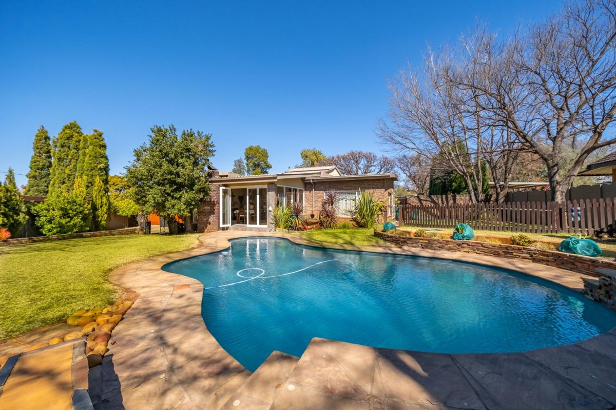 Rear view of the property featuring a well-maintained swimming pool, paved patio area, and landscaped garden with a brick facade.
