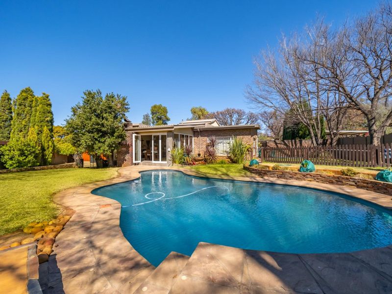 Rear view of the property featuring a well-maintained swimming pool, paved patio area, and landscaped garden with a brick facade.