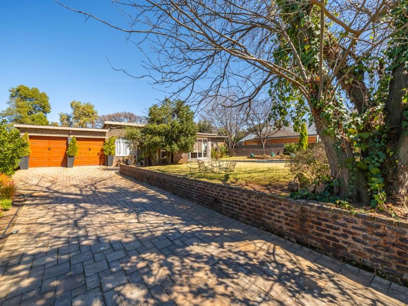 Front exterior view of the property featuring a paved driveway, double garage, and a well-maintained front garden with a brick retaining wall.
