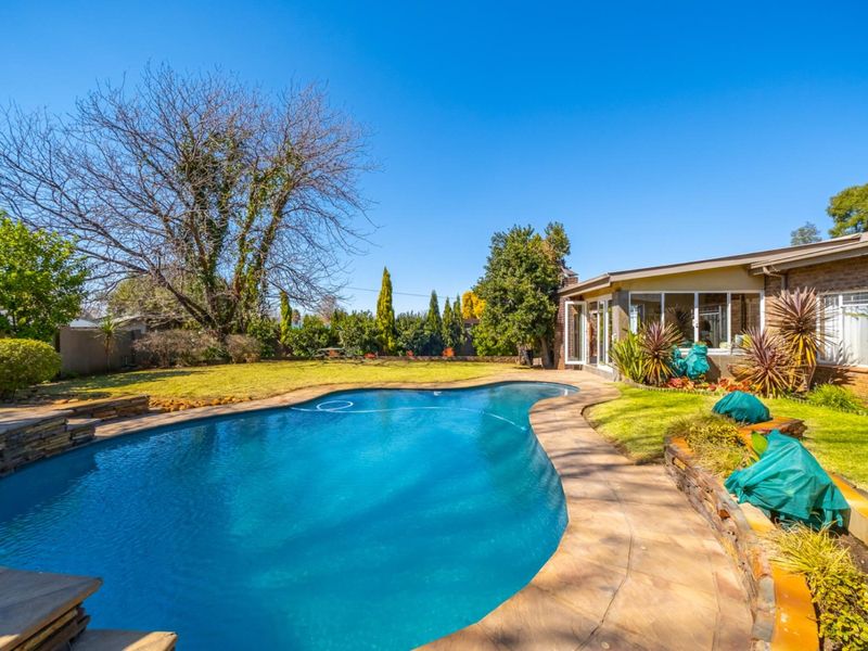 A well-maintained backyard featuring a curved swimming pool with stone paving, a landscaped lawn, and direct access to the home via sliding glass doors.