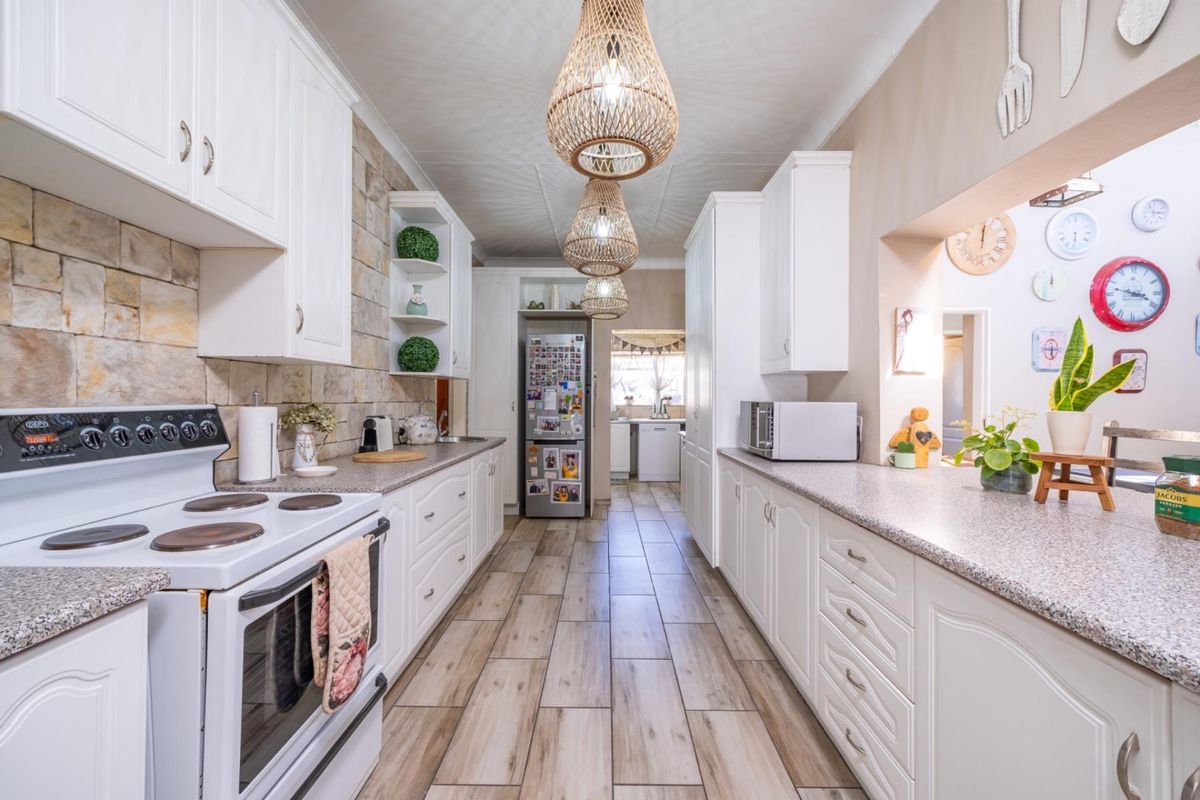 A well-maintained galley-style kitchen featuring white cabinetry, stone-look tile backsplash, laminate countertops, and tiled flooring with a view into the scullery area.