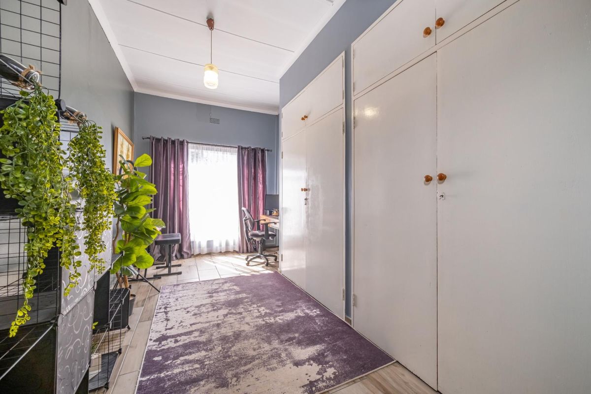 A bedroom featuring extensive built-in cupboards, tiled flooring, and natural light, offering a functional space with potential for modern updates.