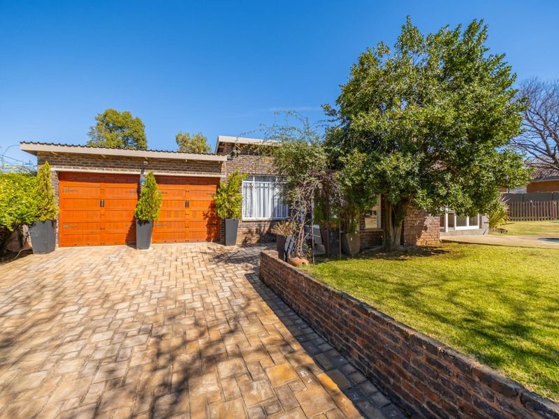 Front view of the property featuring a double garage, paved brick driveway, and a well-maintained front garden with a brick retaining wall.