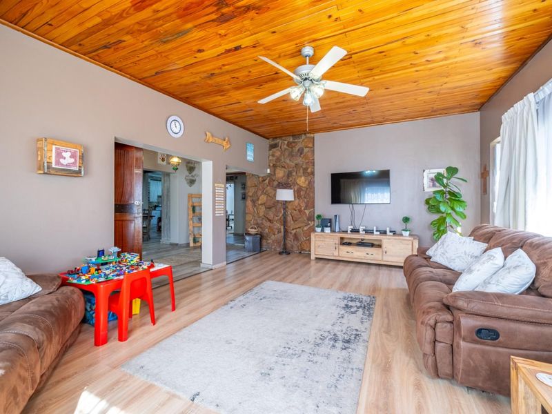 Spacious living room featuring a warm timber-clad ceiling, a rustic stone feature wall, and durable laminate flooring with access to adjacent living areas.