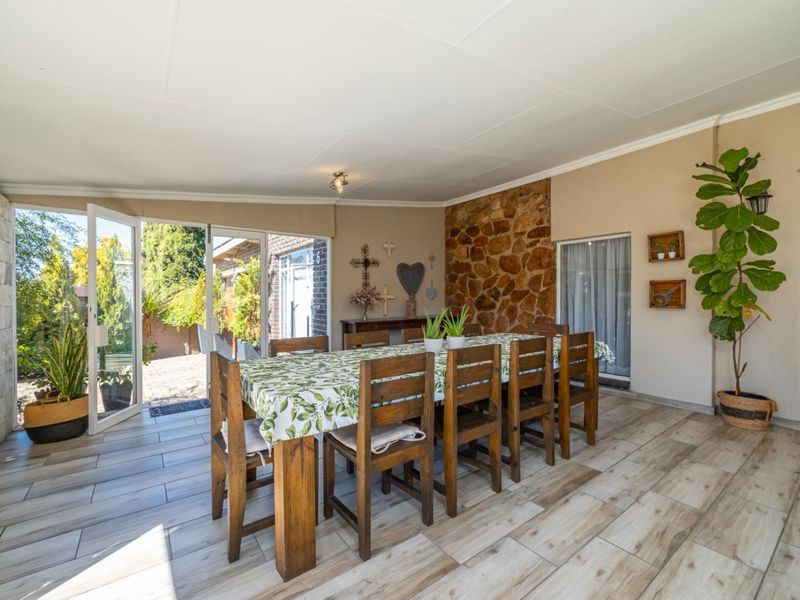 A spacious covered patio area featuring a stone accent wall, wood-look tiled flooring, and large sliding glass doors providing access to the garden.