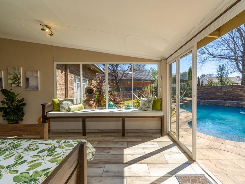 A bright, enclosed patio area featuring large sliding glass doors that open directly onto the swimming pool and garden area.