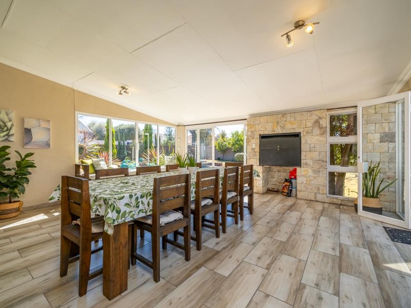 Spacious enclosed patio featuring stone cladding, a built-in braai, and large glass sliding doors that provide ample natural light and garden views.
