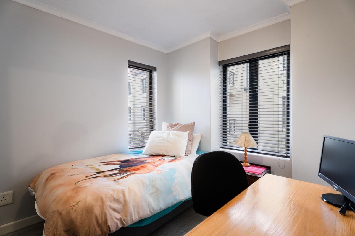 A well-lit bedroom featuring neutral walls, coving, and dual windows fitted with venetian blinds, providing a functional and comfortable living space.