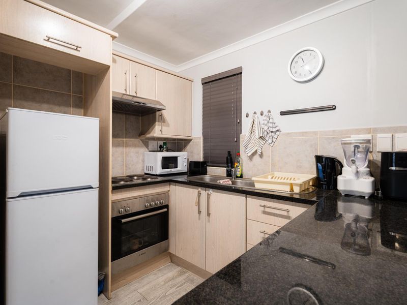 Compact kitchen featuring light wood cabinetry, dark granite countertops, built-in oven, electric hob, and tiled backsplash.