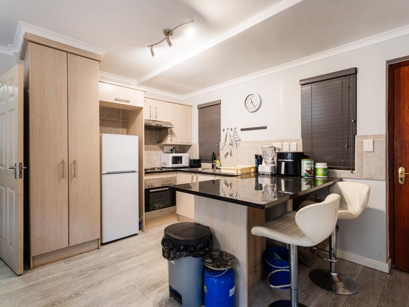 A functional kitchen featuring light wood cabinetry, granite countertops, integrated oven and hob, and modern laminate flooring with neutral wall finishes.