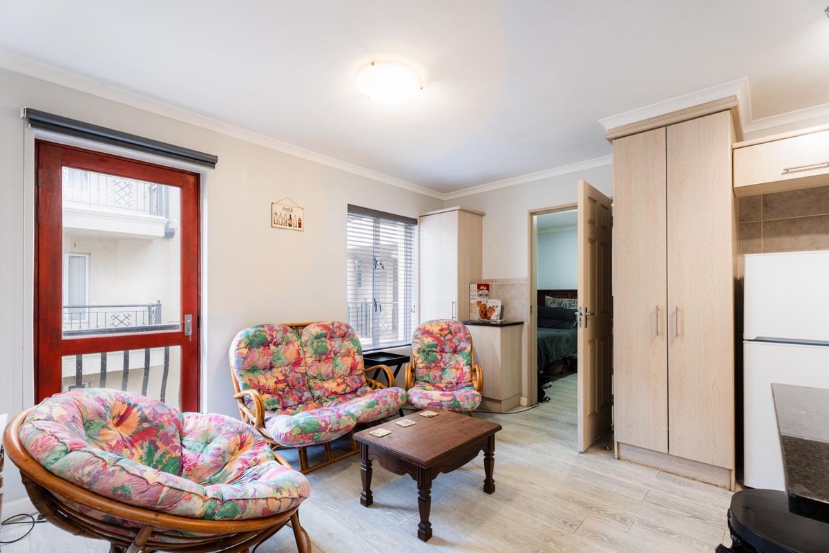 A living area featuring laminate flooring, built-in cabinetry, and access to an adjacent bedroom and balcony.