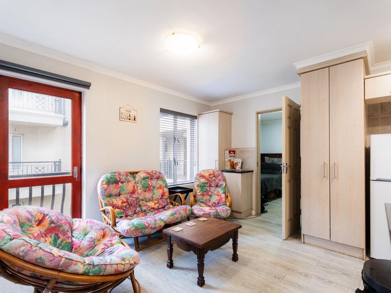 A living area featuring laminate flooring, built-in cabinetry, and access to an adjacent bedroom and balcony.