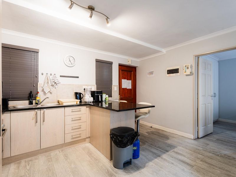 A functional kitchen featuring light wood-finish cabinetry, granite countertops, a tiled backsplash, and modern laminate flooring with integrated track lighting.