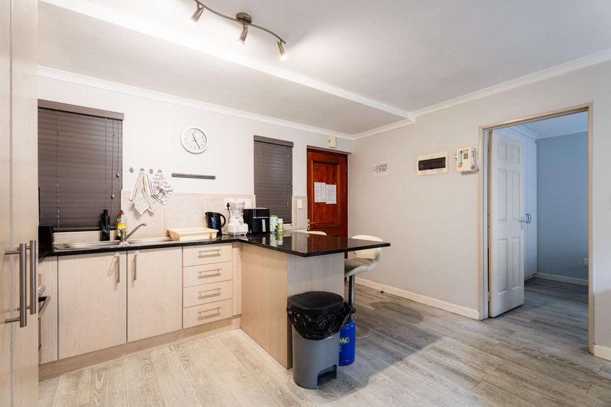A functional kitchen featuring light wood-finish cabinetry, granite countertops, a tiled backsplash, and modern laminate flooring with integrated track lighting.