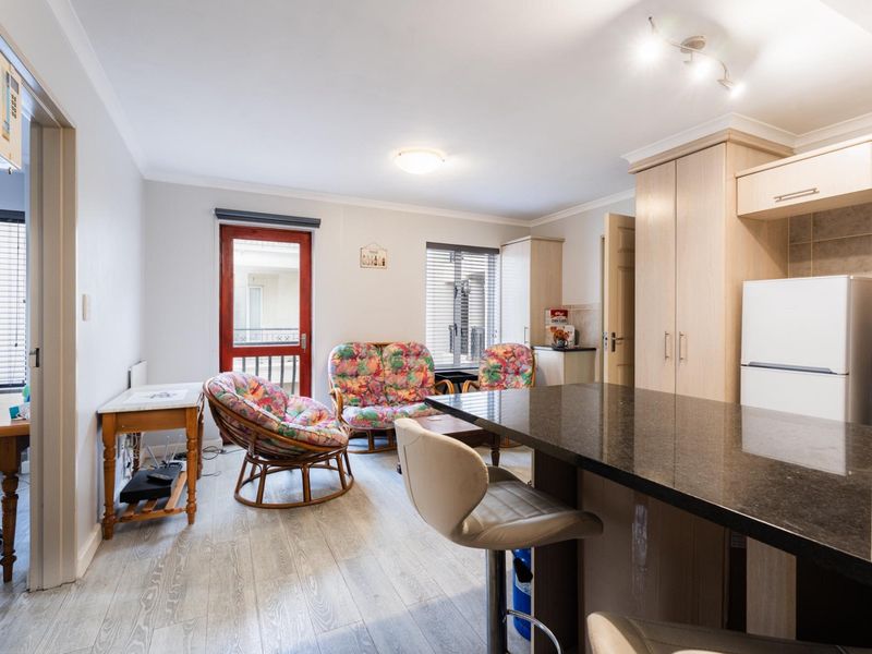 Open-plan living and kitchen area featuring a granite island, light wood cabinetry, and direct access to a balcony through a glass panel door.