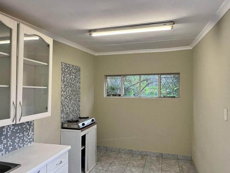 A functional kitchen space featuring built-in cabinetry, a mosaic tile splashback, gas cooktop, and tiled flooring with natural light from a diamond-patterned window.