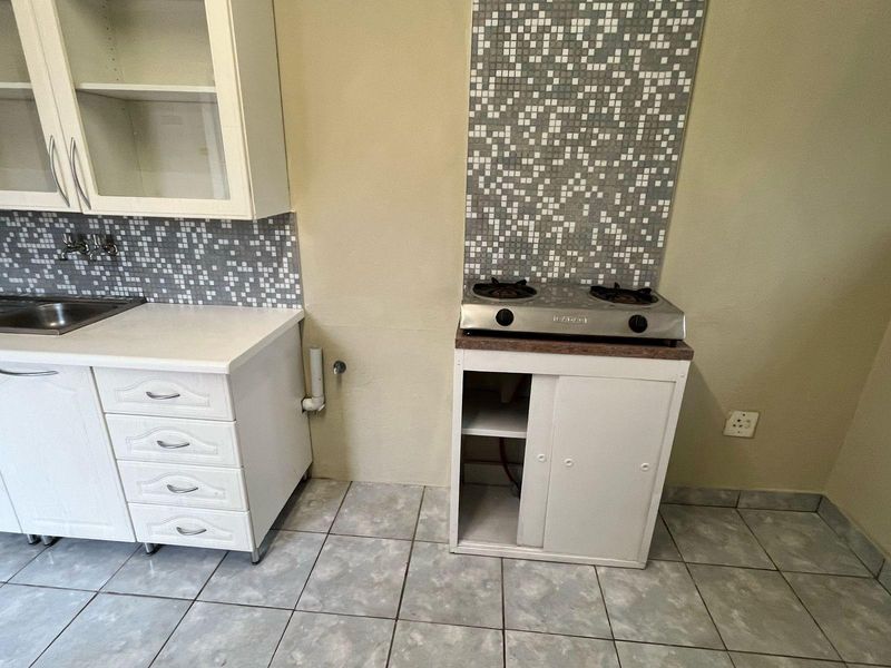 A compact kitchen area featuring white cabinetry, a mosaic tile backsplash, a stainless steel sink, and a gas cooktop with tiled flooring.